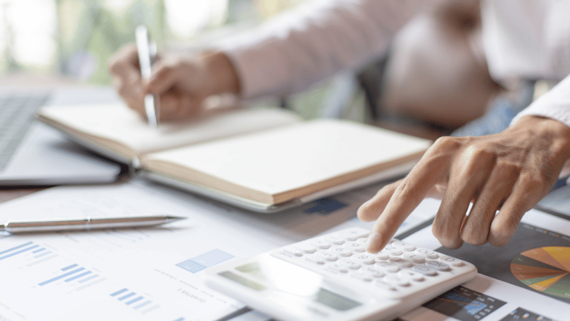 Blog20Covers20-202023-03-21T153857.588 Woman looking at business analytics and making calculations using a calculator and notebook