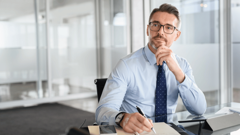 Confident businessman wearing glasses while sitting at a desk taking notes