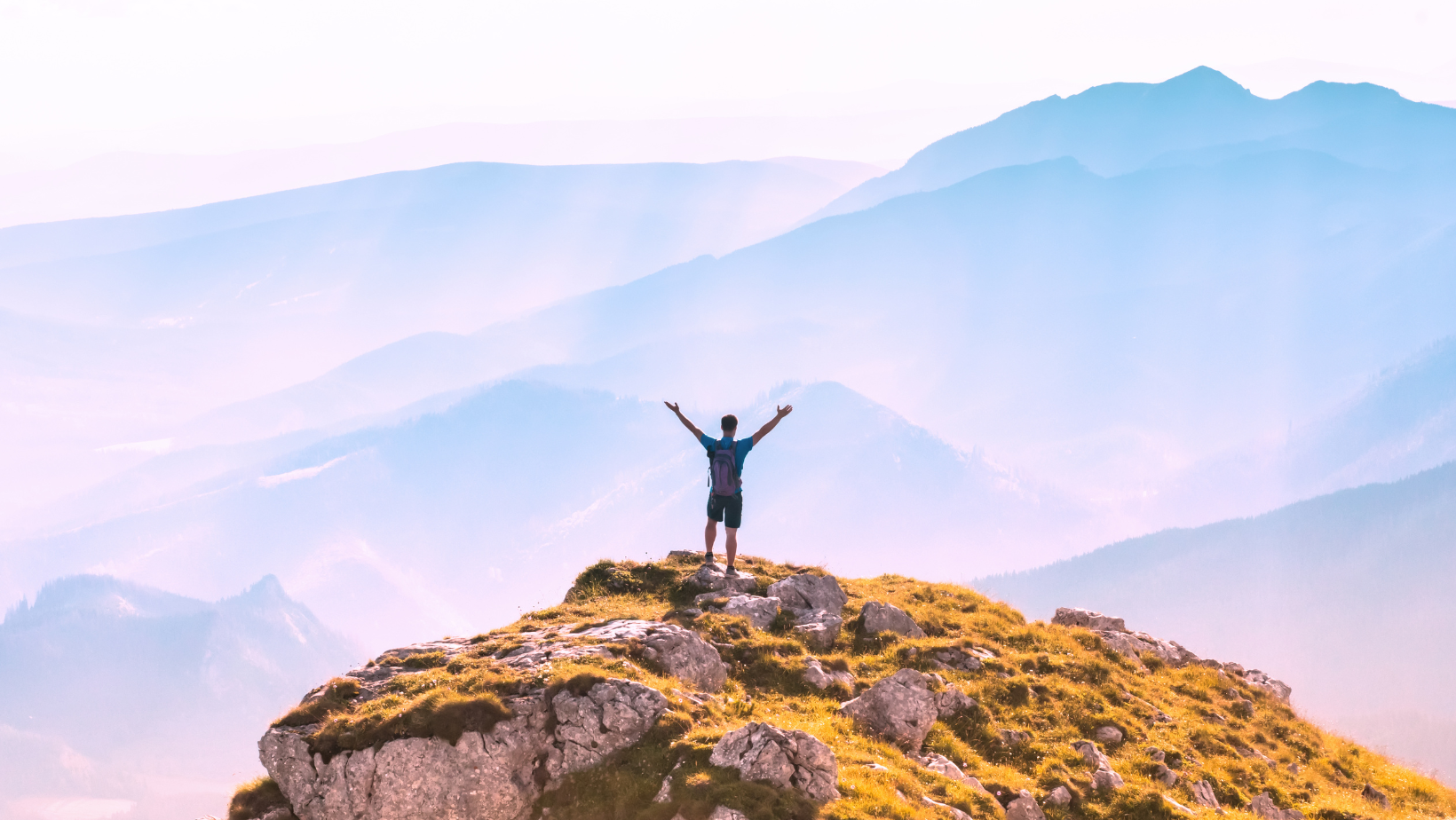 Blog20Covers20284729-2 Aspirational image of a young man at the top of a mountain with his arms up in celebration