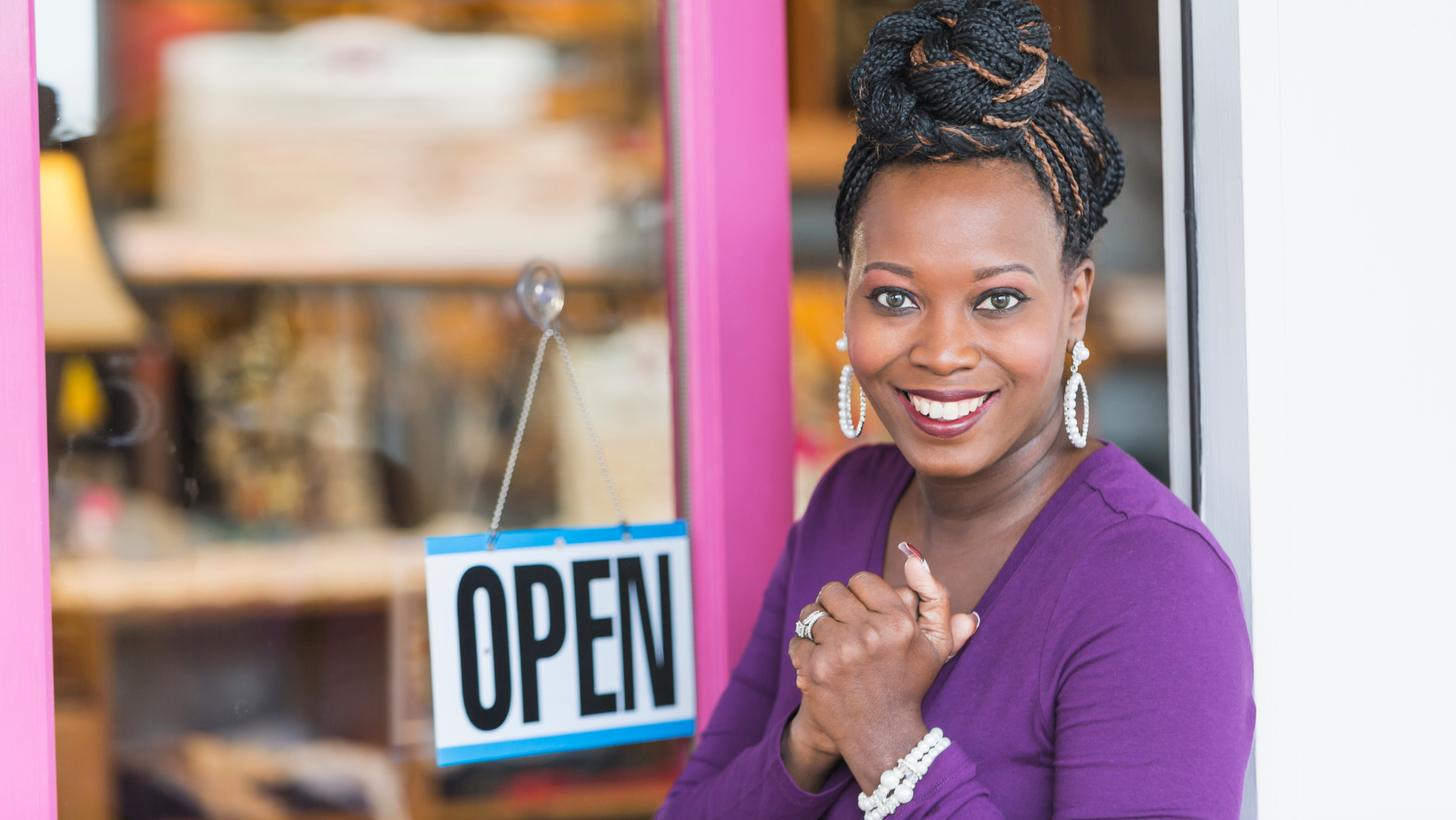Excited Black female entrepreneur outside a pink office space with an OPEN sign