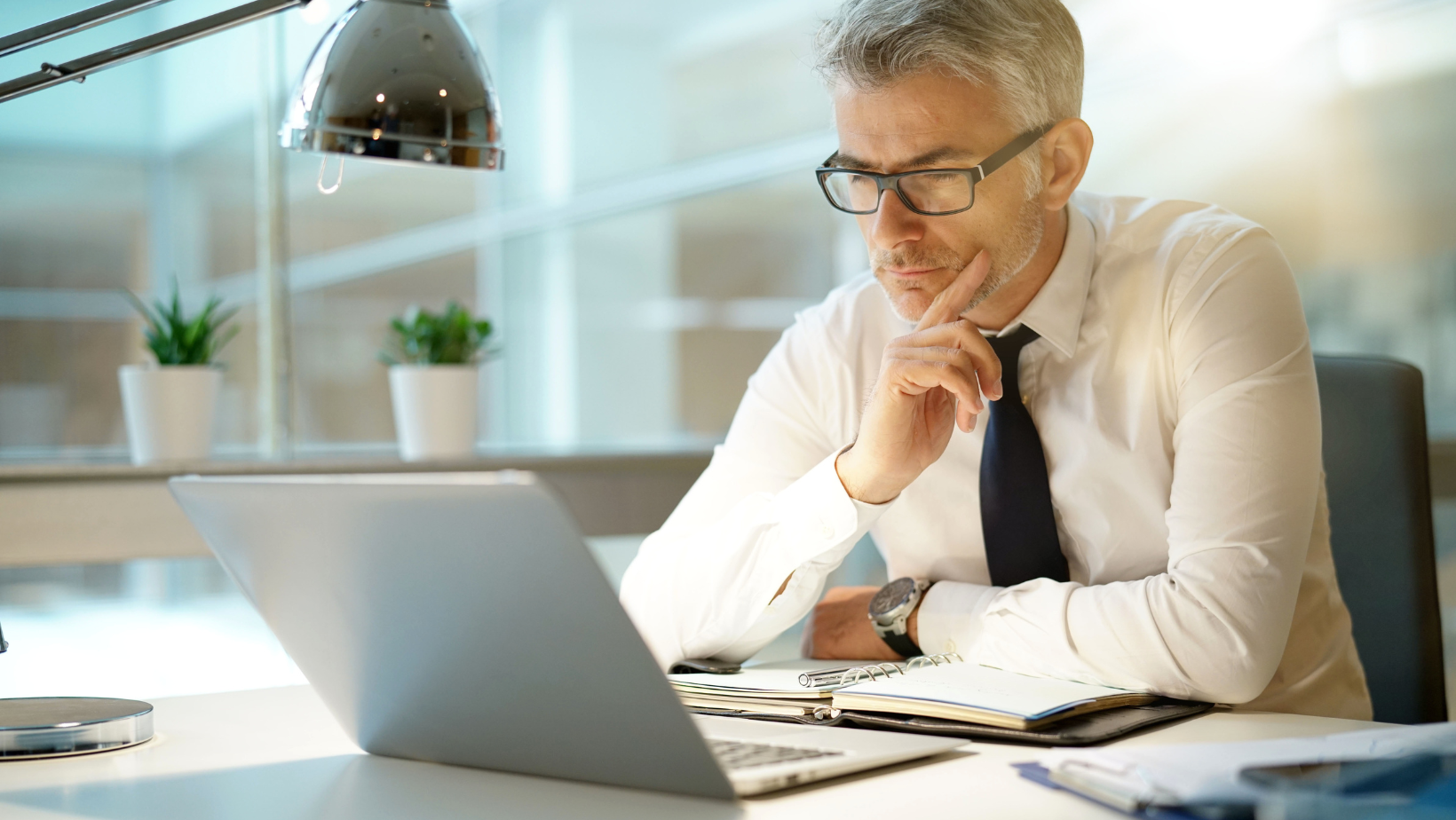 Businessman wearing glasses and sitting at his desk with an open laptop and daily planner