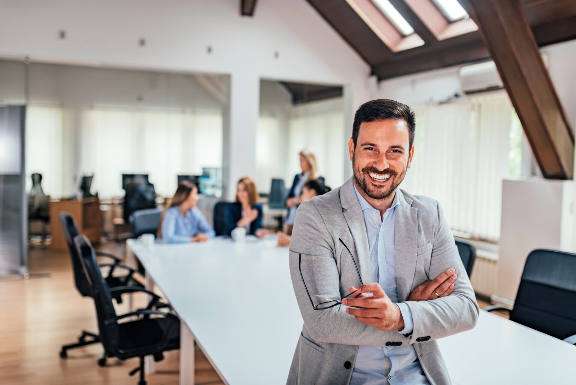 Handsome executive smiling in the office, with colleagues in background. Handsome executive smiling in the office, with colleagues in background.