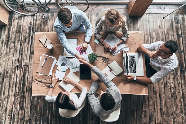 Top view of young modern men in smart casual wear shaking hands while working with their colleagues in the creative office