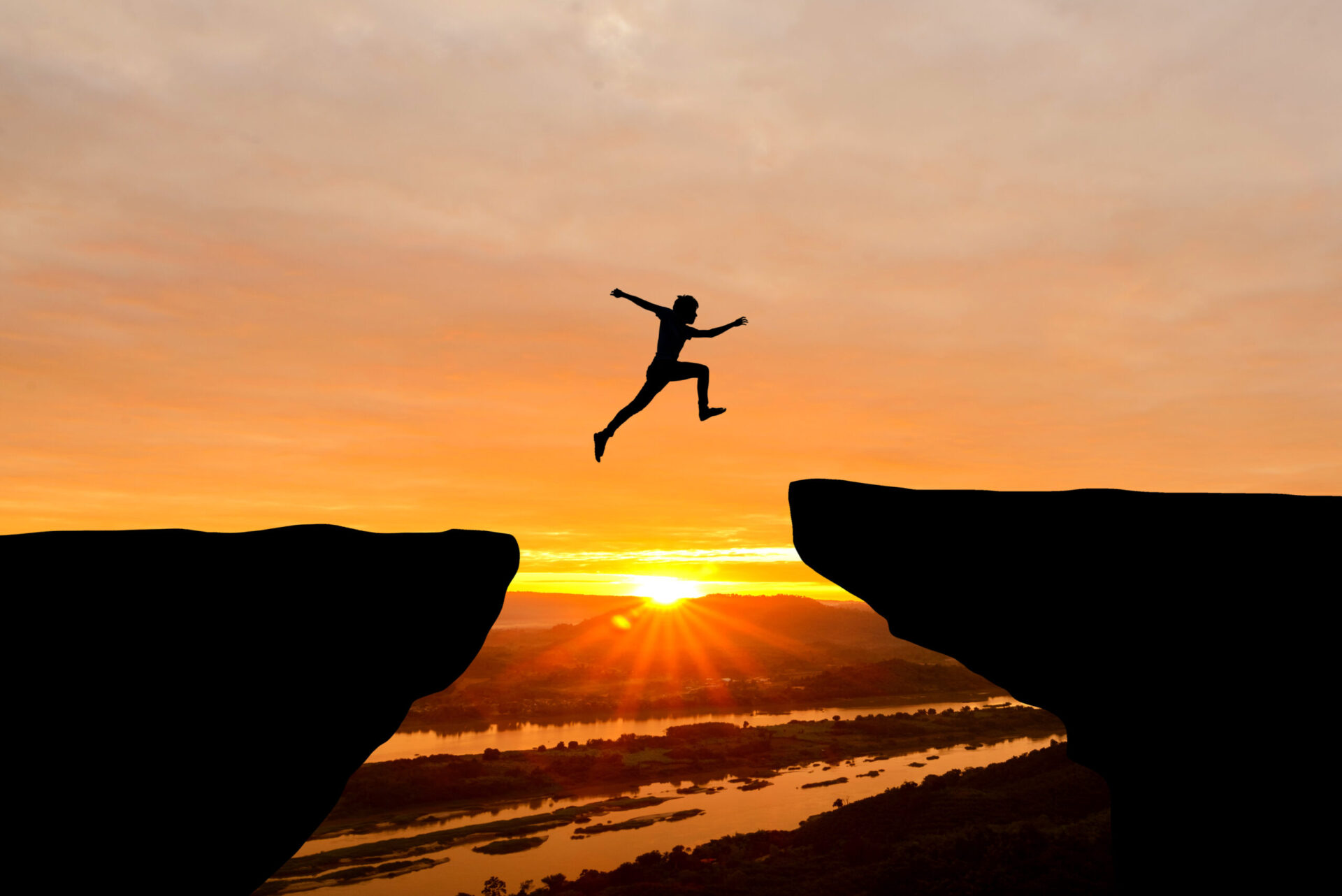 Man jumping over cliff on sunset background