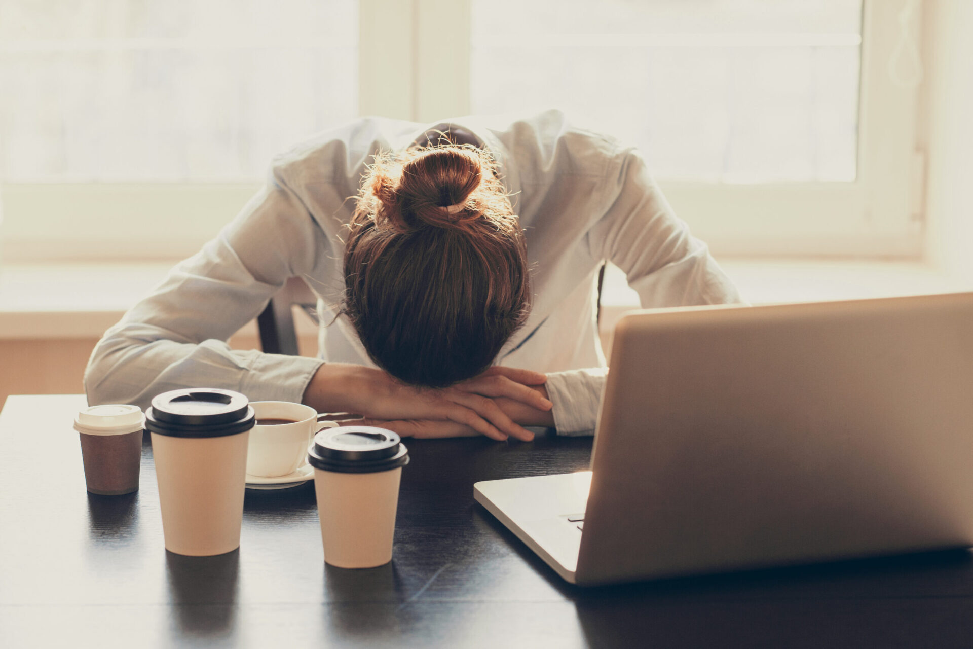 Stressed businesswoman in the office. Tired woman working at home. Business, stress, people, depression, pressure, career, crisis, problems concept Stressed business woman with her head on the table next to her laptop and several cups of coffee