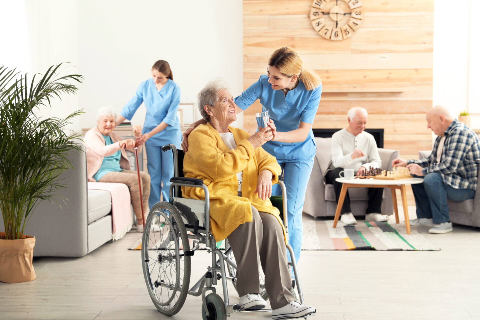 Nurse giving glass of water to elderly woman in wheelchair at retirement home.
