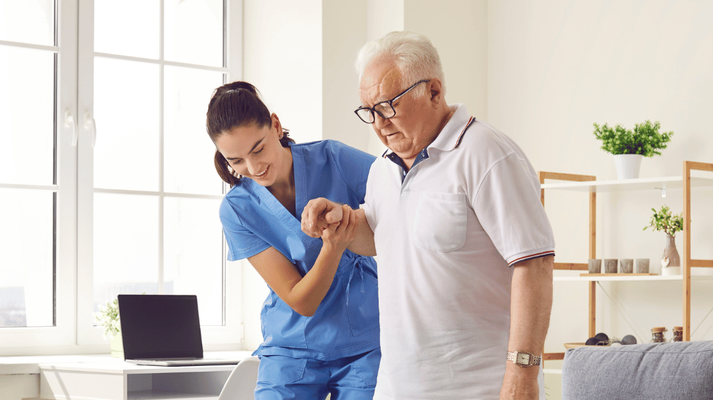 Blog Covers – 2025-03-27T131408.032 Caregiver assisting a senior man with walking in his home