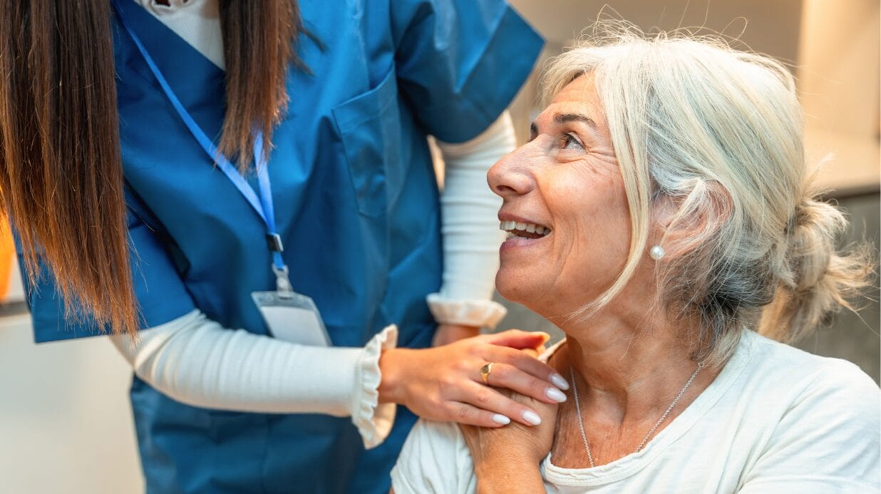 Blog Covers (5) Caregiver with her hand on the shoulder of a senior woman, who is smiling up at the caregiver