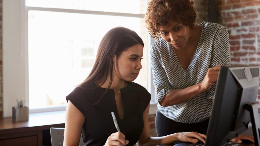 Blog Covers (24) A professional taking training courses with a mentor helping her at a computer