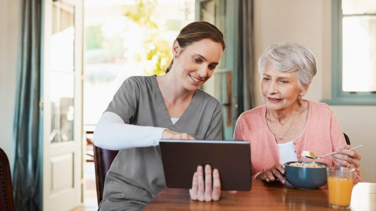 Blog Covers (54) Senior caregiver helping a senior with a tablet while she eats breakfast